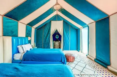 two beds in a room with blue walls at Merzouga Luxury Camp & Desert Activities in Merzouga