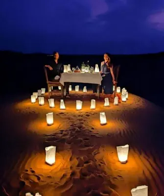 two people sitting at a table on the beach at night at Merzouga Luxury Camp & Desert Activities in Merzouga