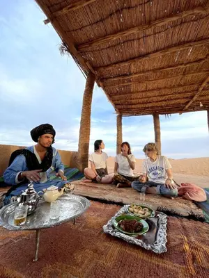 a group of people sitting on the beach eating food at Camp Nuyum in Ksiba