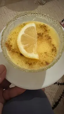 a person holding a cup of coffee with a lemon in it at Merzouga Desert Camping in Hassilabied