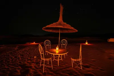 a table with chairs and an umbrella on the beach at night at Merzouga Desert Camping in Hassilabied