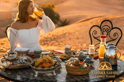a woman drinking a glass of orange juice at a table in the desert at Sahara Safari Luxury Tented in Merzouga