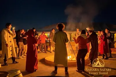 a group of people standing around a fire at Sahara Safari Luxury Tented in Merzouga