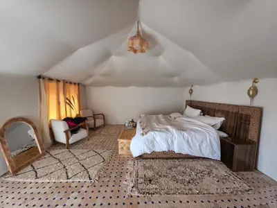 a bedroom with a bed and a chair in a room at Noor Dunes Camp in Merzouga