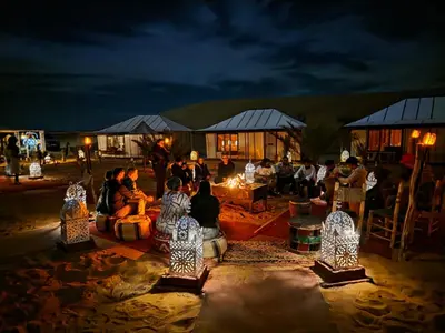 a group of people sitting around a fire at night at Noor Dunes Camp in Merzouga