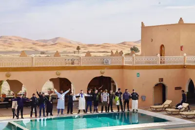 a group of people standing next to a swimming pool at Hotel Sunset palace Merzouga in Merzouga