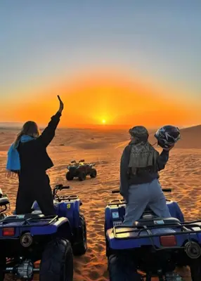 two people are standing on atvs in the desert at Hotel Sunset palace Merzouga in Merzouga