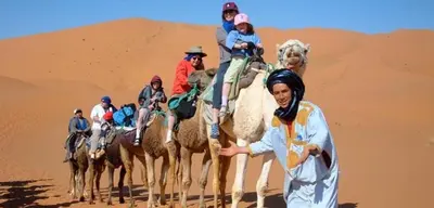 a group of people riding camels in the desert at Merzouga Sunshine traditional luxury camp in Merzouga