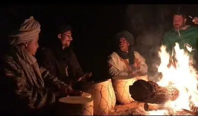 a group of people sitting around a fire at Merzouga Sunshine traditional luxury camp in Merzouga
