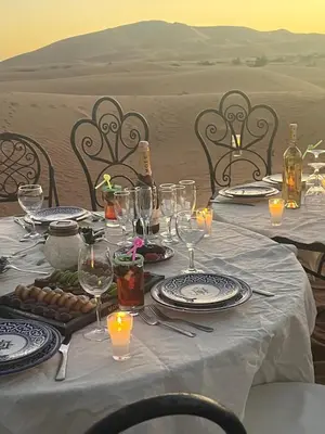 a table with plates and wine glasses in the desert at Erg Chebbi Luxury Glamping in Khamliya