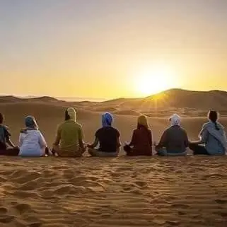 a group of people sitting in the desert watching the sunset at Erg Chebbi Luxury Glamping in Khamliya