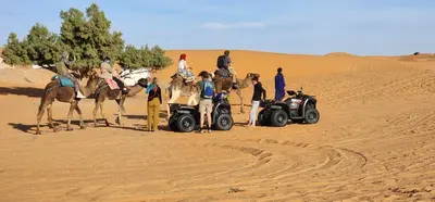 a group of people and a atv in the desert with a camel at Hotel oasis merzouga in Merzouga