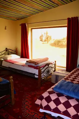 a bedroom with two beds and a large window at Rimal Travel Camp in Mhamid