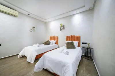two beds in a room with white walls and wood floors at Mina Home 2 in Oulad Akkou