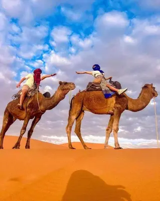 two people riding on the backs of camels in the desert at Andromeda Sahara Camp in Merzouga