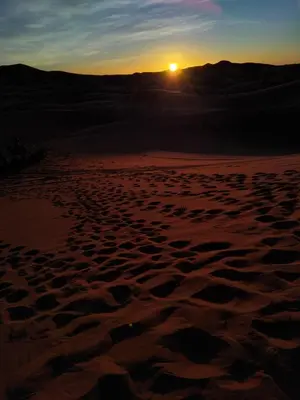 a sunset in the desert with footprints in the sand at Erg Chebbi Dream Camp in Merzouga