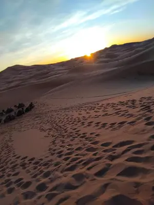 a sunset in the desert with footprints in the sand at Erg Chebbi Dream Camp in Merzouga