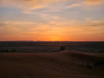 a sunset in the desert with the sun setting in the distance at Itran desert camp in Merzouga