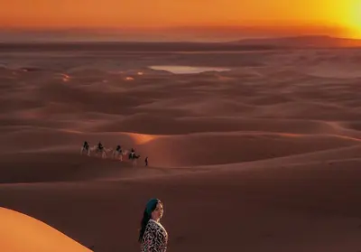 a woman standing in the desert with a group of people riding horses at Brilliant luxury camp in Merzouga
