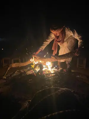 a man standing next to a fire in the dark at Desert Family Camp in El Gouera