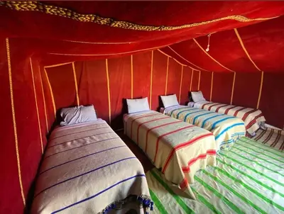 a group of four beds in a red tent at Milky Way Chigaga Camp in El Gouera