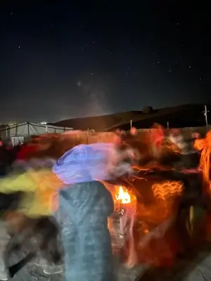 a group of people with umbrellas standing around a fire at Sahara Joy Camp in Merzouga