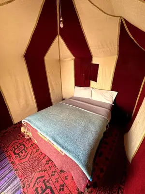 a small bed in a room with a red wall at Sahara Joy Camp in Merzouga