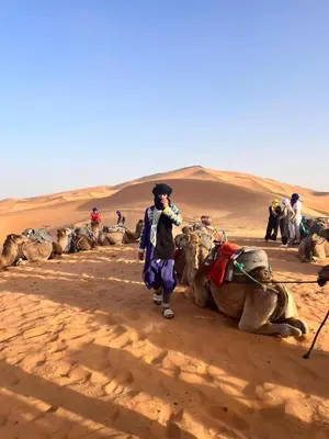 a man standing next to a camel in the desert at Sahara Luxury Camp in Merzouga