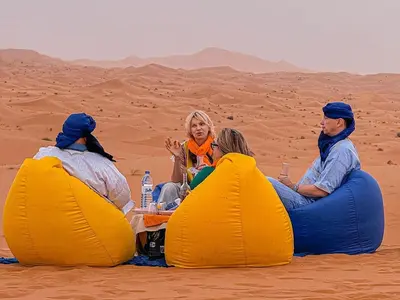 three people sitting in the desert eating food at Maria'S Luxury Camp in Merzouga