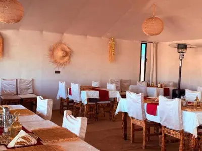 a dining room with tables and chairs with white tables and white chairs at Dream Land Camp in Merzouga