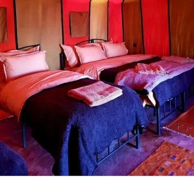 two beds in a room with red and blue at Chebbi Desert Camp in Merzouga