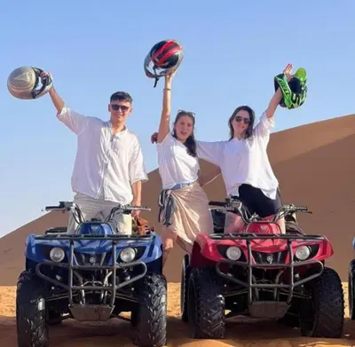 three people holding up their atvs in the desert at Chebbi Desert Camp in Merzouga