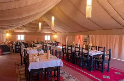 a dining room with tables and chairs in a tent at Chebbi Desert Camp in Merzouga