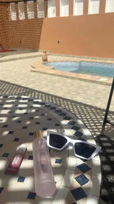 a pair of sunglasses and a bottle of sunscreen next to a swimming pool at Apartment with Pool & Kasbah View in Aït Ben Haddou