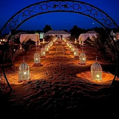 a long aisle with lanterns and lights at night at Mirage Luxury Camp in Merzouga