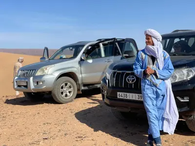 a woman standing next to a car in the desert at Tarrast Desert Camp in Mhamid