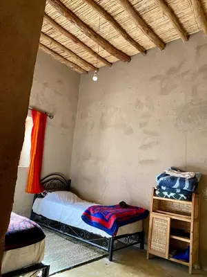 a bedroom with a bed and a table in a room at Merzouga Desert Family Host tata- Hassi Labied Dunes View & Tours in Hassilabied