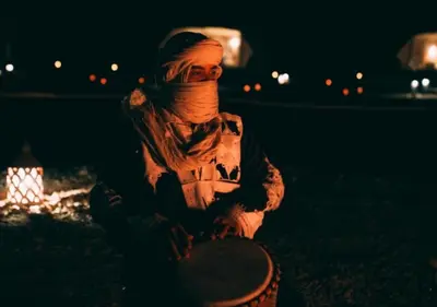 a woman sitting in front of a fire at night at Solaris Luxury Camp in Merzouga
