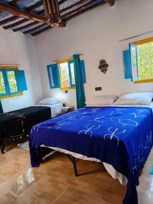 a bedroom with a blue bed in a room with windows at Le Retour au calme Maison d'hôtes in Tinerhir