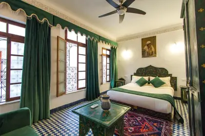 a bedroom with a bed with green curtains and a table at Riad Dar Bab Guissa in Fès