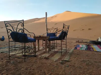 three chairs and a table in the desert at Riad Amar in Merzouga
