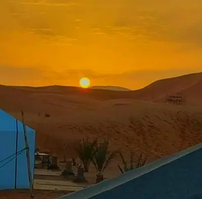 a sunset in the desert with the sun in the sky at Dune Merzouga Camp in Merzouga