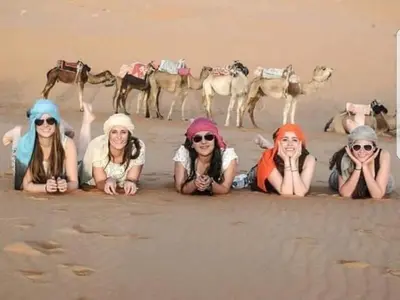 a group of women laying in the sand with their camels at Dune Merzouga Camp in Merzouga