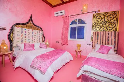 a pink bedroom with two beds and a window at Dar tiwira in Aït Baha