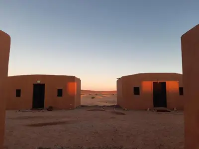 two buildings in the desert with the sunset in the background at Sahara Peace camp in Zagora