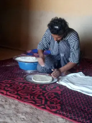 a person sitting on the floor with a plate on a rug at Sahara Peace camp in Zagora