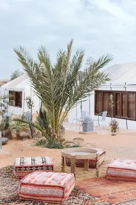 a patio with a table and benches and a palm tree at Caravanserai Luxury Desert Tented Camp in Merzouga
