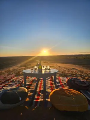 a table in the middle of the desert with a bottle of wine at Riad Marhaba Merzane in Merzane