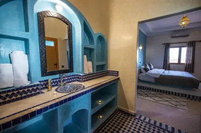 a bathroom with a sink and a mirror and a bed at Riad Les jardins de Merzouga in Merzouga