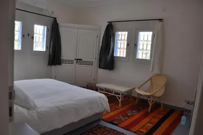 a bedroom with a bed and a chair and windows at Maison La Berberina in Goulmima